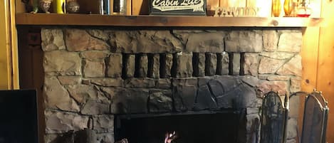 Interior rústico de una cabaña con chimenea de piedra, cabeza de venado montada y una repisa con diversos objetos.