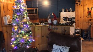 A cozy cabin interior with a wooden interior, a Christmas tree, a leather armchair, and a kitchen area with cabinets and appliances. - Charming Ski cabin with WiFi near Dodge Ridge, great for family or small group. (Mi-Wuk Village)