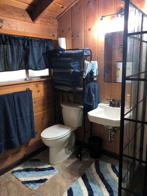 A small, wooden cabin bathroom with a toilet, sink, and stacked towels. - Charming Ski cabin with WiFi near Dodge Ridge, great for family or small group. (Mi-Wuk Village)