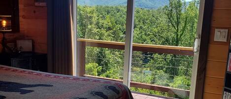 A bedroom with a large bed, a view of a balcony, and a wooden cabin interior.