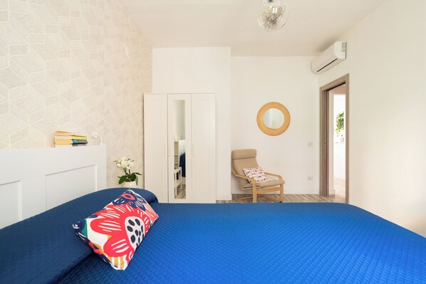 A bedroom with a blue bedspread, a chair, a mirror, and a wardrobe.