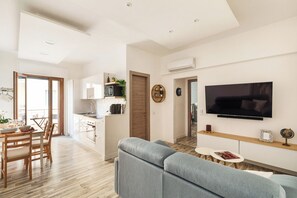 Una sala de estar moderna con un sofá gris, un televisor de pantalla plana y una mesa de comedor de madera con sillas.