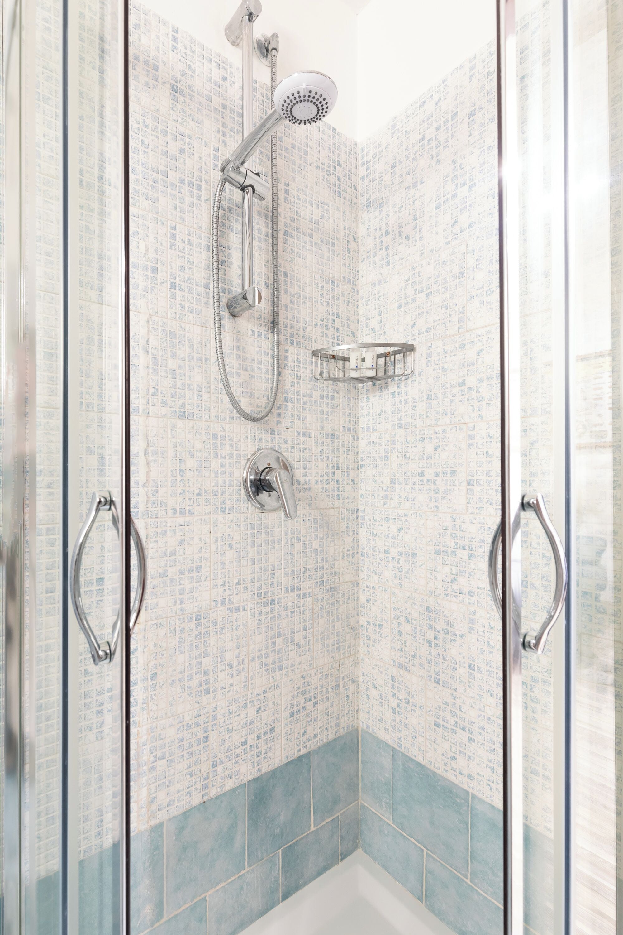 A glass-enclosed shower with a handheld showerhead, a wall-mounted faucet, and a shower tray.