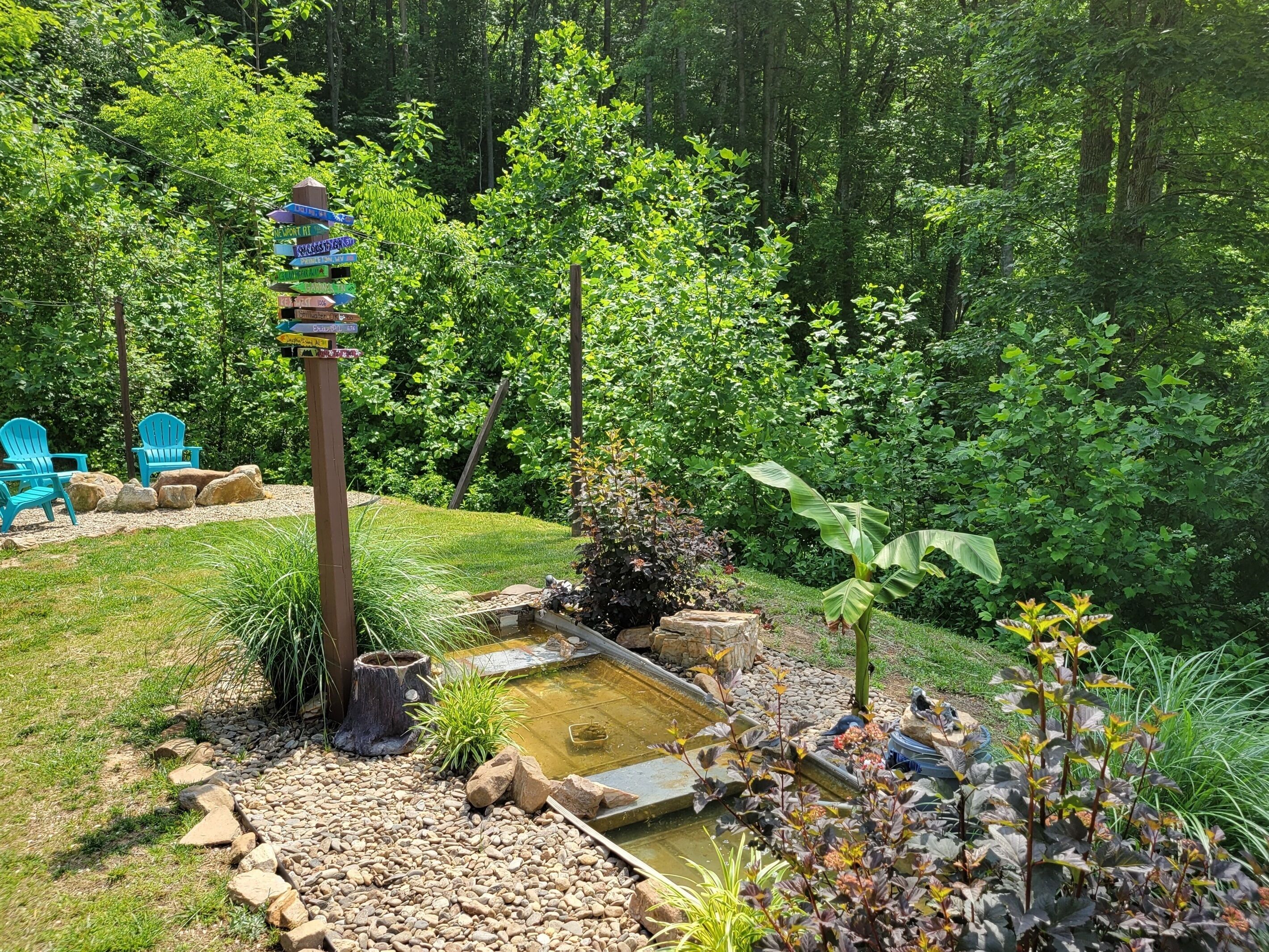 A garden with a pond, chairs, and a signpost.