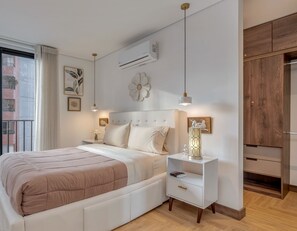 Un dormitorio con cama, mesitas de noche, aire acondicionado, ventana con cortinas y vista a un edificio.