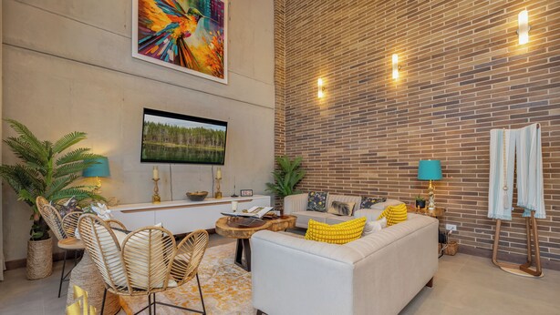 A modern living room with a white sofa, a dining area with wicker chairs, a wooden coffee table, and a brick wall with built-in lighting. - Elegant/Modern Apt in Poblado - Morph 1201 (Medellín)