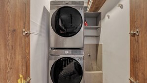 A compact laundry area with two stacked washing machines, wooden doors, and a small shelving unit. - Elegant/Modern Apt in Poblado - Morph 1201 (Medellín)