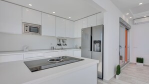 Een moderne keuken met witte kastjes, een inbouwmagnetron, een roestvrijstalen koelkast en een centraal eiland met een kookplaat.