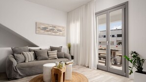 Un salón moderno con un sofá gris, una mesa de centro redonda de madera y un amplio ventanal corredero que da a un espacio exterior.