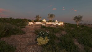 A stone pathway leading to a seating area with a stone wall and lanterns, surrounded by vegetation and trees. - Villa Aether Stelida Naxos (Naxos)