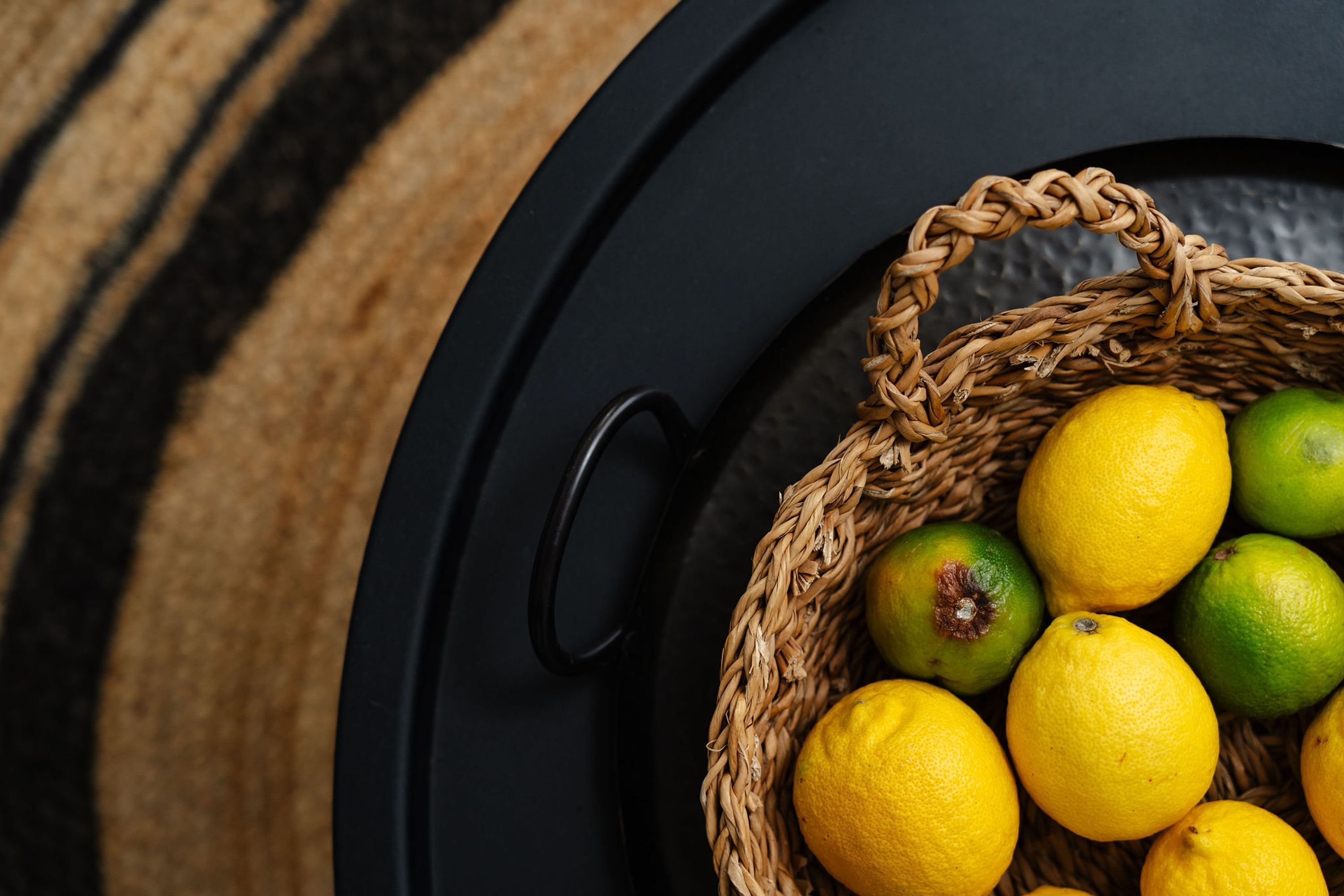 A wicker basket filled with lemons and limes on a black surface.
