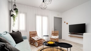 En moderne stue med en sofa, to fletstole, et fjernsyn og et spisebord med en kurv med frugt.