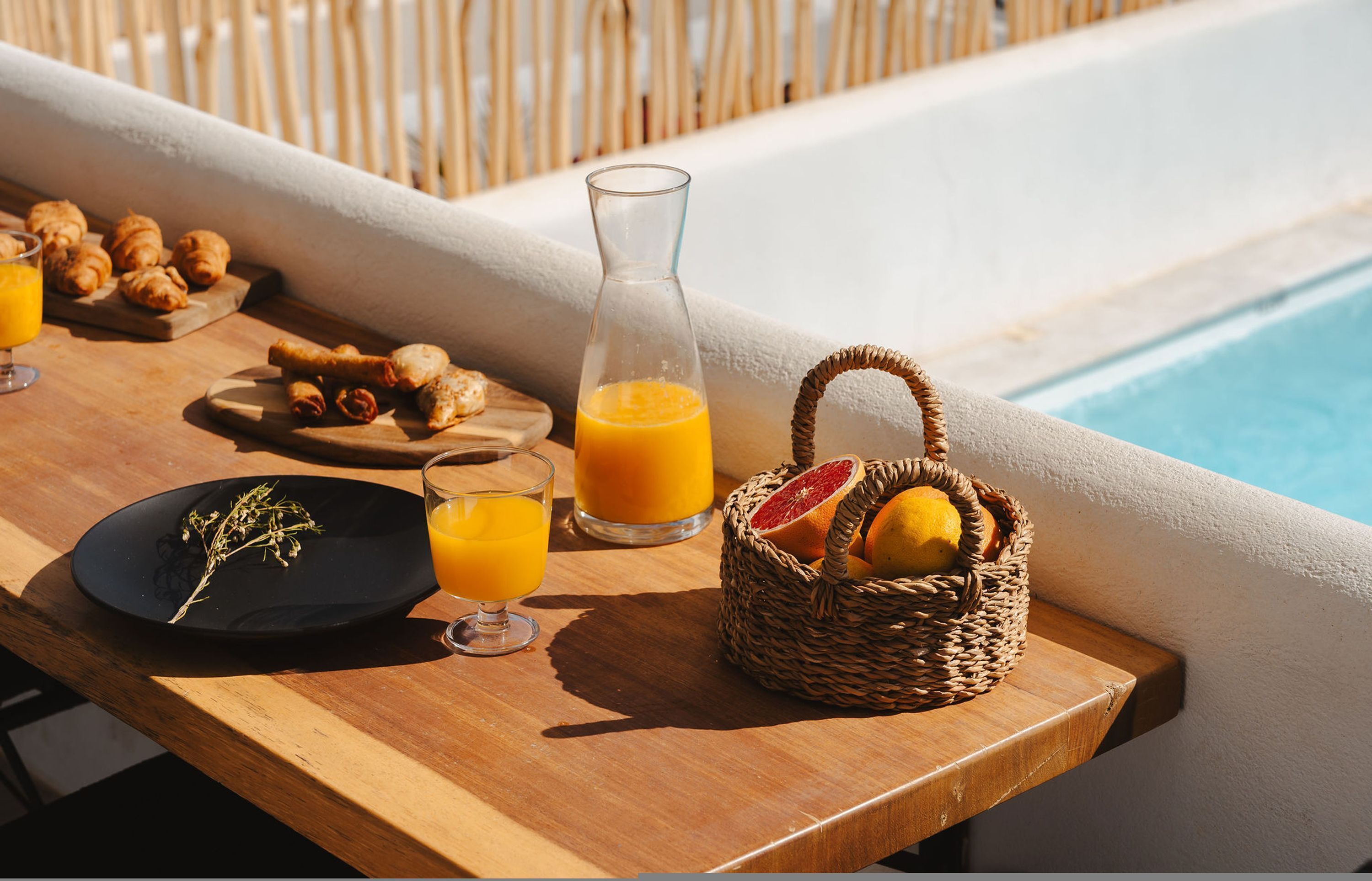 Ein Frühstückstisch am Pool mit Croissants, Orangensaft und einer Obstauswahl.