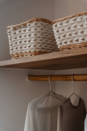A wooden shelf with woven baskets and a clothing rack with garments.