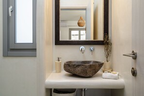 A bathroom with a large stone sink, a mirror, a window, and a towel rack.
