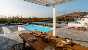 A poolside dining area with a wooden table set for a meal, overlooking a pool and a mountainous landscape. - Villa Kaya Plaka With 3 Bedrooms and 3 Bathrooms (Naxos)