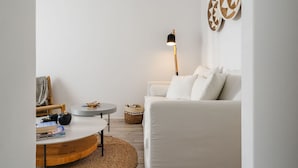 A modern living room with a white sofa, a round wooden coffee table, a floor lamp, and decorative wall art. - Julie s Luxury Apartment (Naxos)