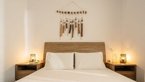 A neatly made bed with white linens, two bedside tables with lamps, and a wooden headboard. - Julie s Luxury Apartment (Naxos)
