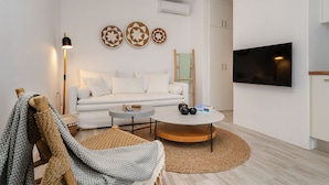 A modern living room with a white sofa, a round coffee table, and a flat-screen TV mounted on the wall. - Julie s Luxury Apartment (Naxos)