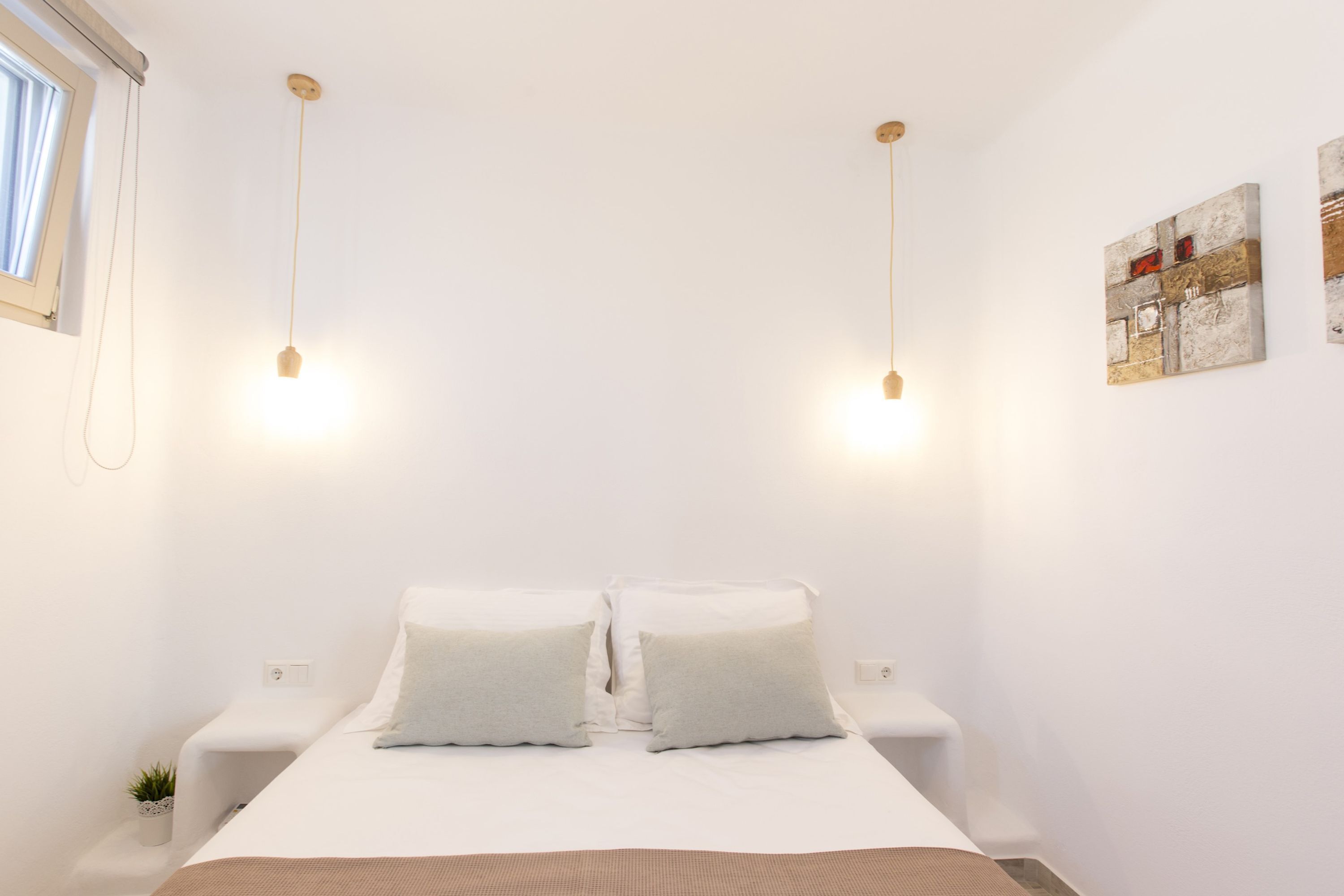 A minimalist bedroom with a large bed, two bedside tables, a small plant, and a wall-mounted artwork.