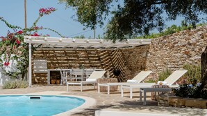 A pool area with lounge chairs, a pergola, stone walls, and a stone bench.