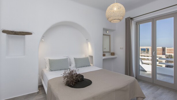 A modern bedroom with a large bed, a hanging light fixture, a view of the city through a large window, and a small wooden shelf.