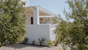 A white building with a pergola, surrounded by greenery and a gravel ground.