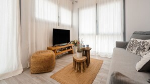 A modern living room with a flat-screen TV, wooden furniture, and large windows with sheer curtains. - Yara sea View Apartment Agia Anna (Naxos)
