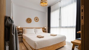 A modern bedroom with a wooden bed, white bedding, two wall decor pieces, and a large window with curtains. - Yara sea View Apartment Agia Anna (Naxos)