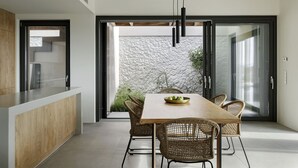 Een moderne keuken met een houten eiland, een eethoek met rieten stoelen en een stenen muur zichtbaar door de glazen deuren.