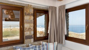 A cozy room with a stone wall, wooden windows, and a view of the sea.