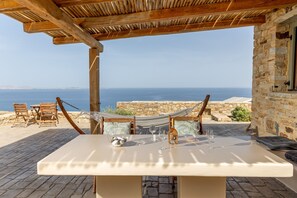 A table set for two with a bottle and glasses, a hammock, and a view of the sea. - Blue View Uphill (Naxos)
