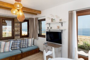 A cozy room with a wooden bench, a TV, and a view of the sea. - Blue View Uphill (Naxos)