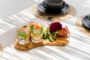 A table with two glasses of water, a wooden board with a dragon fruit, and a black hat.