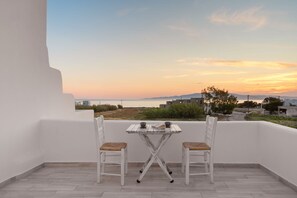 A balcony with two white chairs and a small table, overlooking a coastal landscape during sunset. - Anamnesia Collection Villa Aronia Kastraki Beach (Naxos)