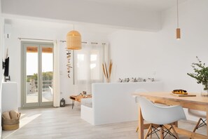 Een moderne, minimalistische woonkamer met een witte bank, een houten eettafel en een groot raam met uitzicht.