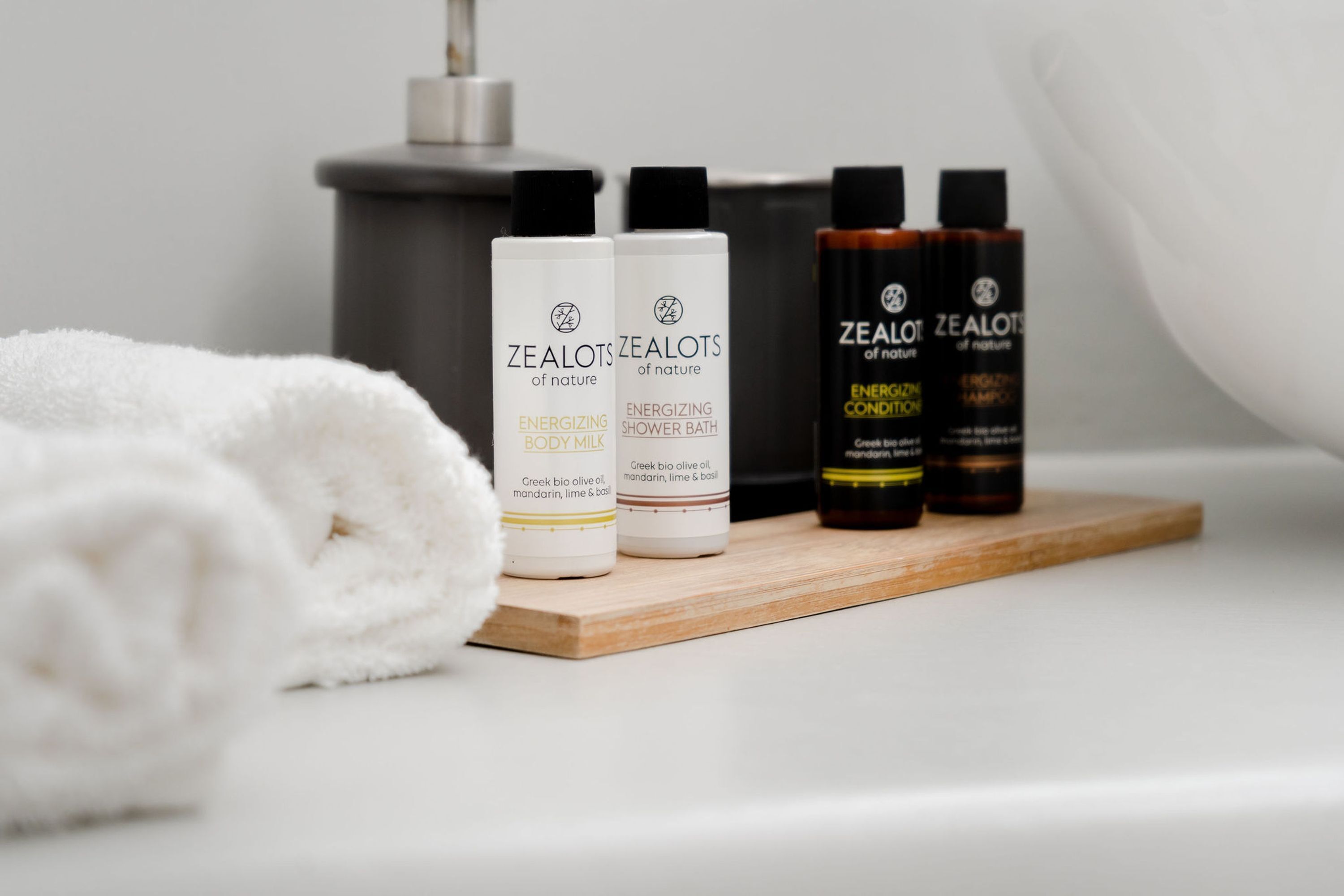 A bathroom with a wooden shelf holding four bottles of Zealots of nature body care products, a white towel, and a showerhead.