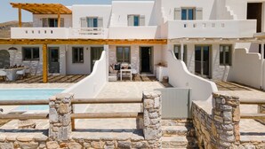 A white building with a pool, stone walls, and outdoor seating.