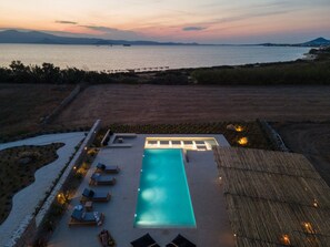 Ein Schwimmbecken mit Liegestühlen und Blick auf das Meer bei Sonnenuntergang.