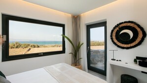 A bedroom with a large window, a bed, a potted plant, a wall-mounted circular decoration, and a small desk with a lamp. - Villa Anamnisis With 5 Bedrooms and 5 5 Bathrooms (Naxos)
