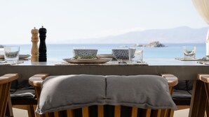 Una mesa de comedor con vista al mar, un salero y pimentero, y un cuenco de hierbas.