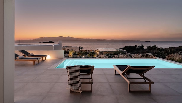 Área de piscina en la azotea con sillas de descanso y vista al océano al atardecer.