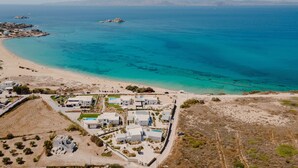 Vista aérea de un complejo turístico costero con villas modernas, una playa y aguas azul cristalino.
