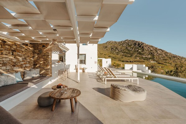 A modern outdoor lounge area with stone walls, a pool, and a mountain view. - 291424 - Villa Flo in Naxos (Naxos)