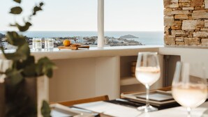 Un coin repas avec vue sur la mer, un mur en pierre et une table dressée avec des verres et un panier de fruits.