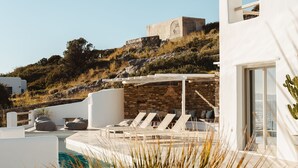 Un espace piscine moderne, doté de chaises longues, d’un mur en pierre et offrant une vue sur une colline.