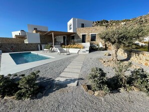 A modern villa with a swimming pool, stone walls, and a garden with olive trees.