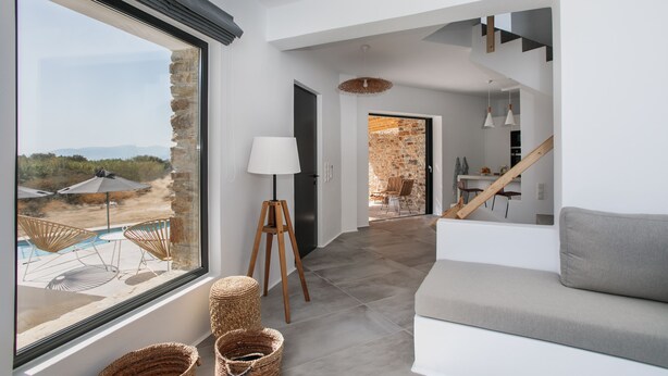 A modern living room with a large window, a sofa, wicker baskets, and a lamp. - Villa Andalusia With 4 Bedrooms and 3 5 Bathrooms (Naxos)