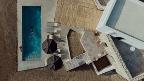 An aerial view of a pool area with a diving board, lounge chairs, and umbrellas.