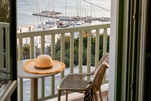 A balcony with a view of a marina, a straw hat on a table, and a wicker chair.